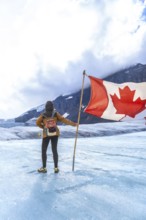 Tourist is holding large canadian flag while standing on athabasca glacier in jasper national park,