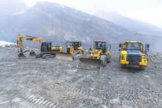 Excavator, bulldozer, and dump truck parked on gravel near athabasca glacier, highlighting