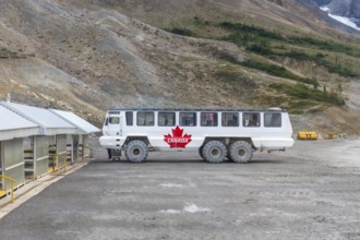 Large all terrain ice explorer bus, adorned with a canadian flag, parked near athabasca glacier in