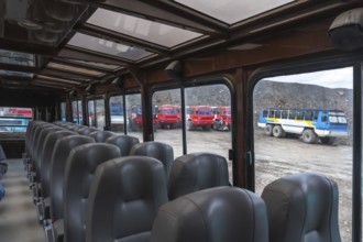 Inside a tour bus at the athabasca glacier, rows of empty gray seats are visible, with large