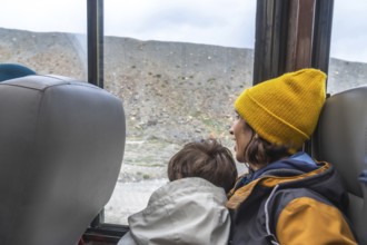Mother and son are enjoying the view of athabasca glacier from a bus window during a sightseeing