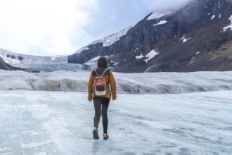Tourist with a backpack walking across athabasca glacier in jasper national park, capturing the