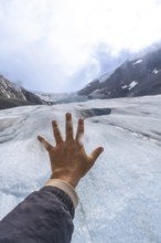 Tourist extends their hand towards the athabasca glacier, part of the columbia icefield in jasper