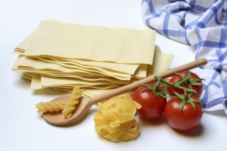 Lasagna, dried lasagna leaves, fusilli and fettuccine noodles with tomatoes and cooking spoon