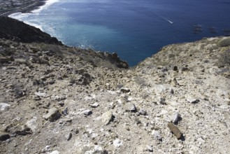 View of the deep blue sea from a rocky slope, with the coast running in the background, Los