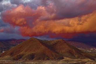 Dramatic cloud formations in shades of red over a mountainous landscape at sunset, Los Cristianos