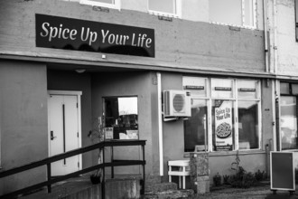 Exterior view of a restaurant with the sign 'Spice Up Your Life' in black and white, daisies