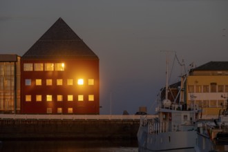 Atmospheric harbor scene with Vardö City Council at sunset with warm light reflections on the