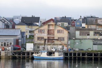 A fishing boat is lying in front of old wooden houses in a quiet harbor, surrounded by morning