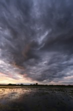 Dramatic cloud atmosphere over flooded wetlands with wind turbines in the background and bright