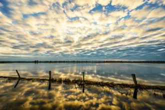 Sky with dramatic clouds is reflected in calm water at sunset, creating a peaceful and impressive
