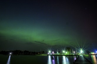 Glowing polar lights in shades of purple and green in front of an illuminated harbor on Lake