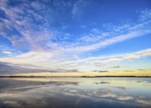 Extensive landscape with blue skies and clouds reflected in the water, soft yellow light on the
