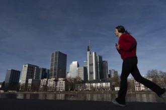 A female jogger walks past the banks of the Main in front of Frankfurt's banking skyline, Mainufer,