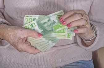 An elderly woman's hands holding Swedish 200-krona banknotes