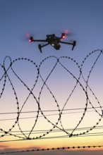 Icon image, illuminated drone hovering over barbed wire at late sunset, airport, threat, espionage