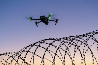 Symbolic picture, illuminated drone flying over barbed wire against the evening sky, airport,