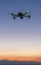 Drone floats in soft evening sky with green lights