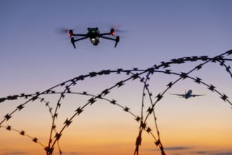 Symbolic picture, drone and airplane in the sky over barbed wire at sunset, airport, threat,