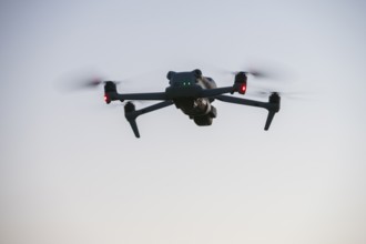 Flying drone with illuminated propellers at dusk