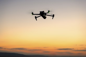 Drone in silhouette flying in front of a colorful sunset