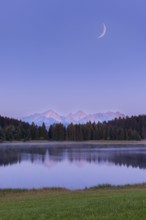Quiet lake in front of mountains and forest with a narrow moon in the sky, Hegratsrieder See near
