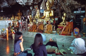 Buddha statue, monks and believers praying, Wat Tam Sua monastery near Krabi, Thailand, December
