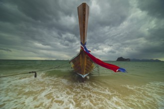 Longtail boat on the beach with dark rain clouds behind it, Koh Ngai island, Andaman Sea, Satun