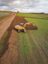Excavator moves soil over a wide field under cloudy sky, Energiewende, construction of PV open