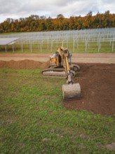 Excavator works near solar plant construction racks, energy transition, construction of PV open
