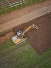Excavator shapes the earth on a large field viewed from above, Energiewende, construction of PV