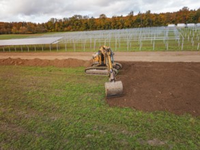 Excavator working near solar panel structures with autumn leaves in the background, energy