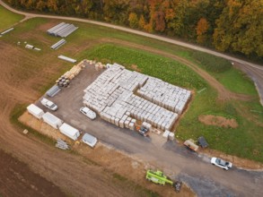 Warehouse with building materials and vehicles, surrounded by fields and an asphalted road, energy
