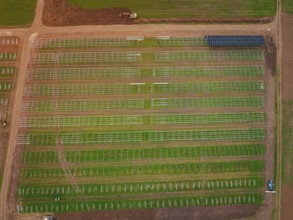 Large-scale solar frame construction on a field, surrounded by farmland seen from the air, energy