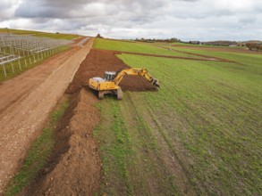 Yellow excavator shovels soil and redesigns the field, energy transition, construction of PV open