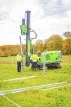 Two workers set up posts in a meadow with a drilling rig, Energiewende, construction of PV open
