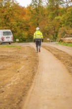 A worker in safety clothing walks on a dirt road through an autumn landscape, Energiewende,