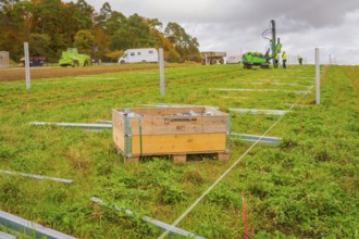A wooden box in a meadow with building elements, surrounded by green grass and autumn landscape,