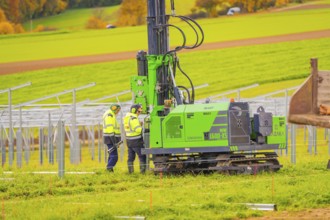 Workers in safety vests monitor the installation of metal structures in an open field,