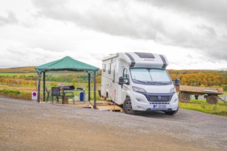 A motorhome with a small pavilion on a hill in front of an autumn landscape, Energiewende,