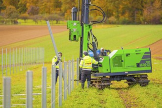 Green machine and worker installing metal poles in the field on a sunny autumn day, Energiewende,