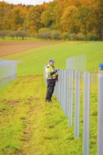 Worker attaches a pole in a row of fields surrounded by colorful autumn leaves, energy revolution,