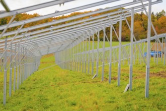 A long metal framework runs on a green field in autumn, surrounded by trees, energy transition,