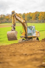 Excavator lifts soil in a green landscape with autumn trees, energy revolution, construction of PV