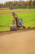 Excavator works on a hill in a green field in autumn, energy revolution, construction of PV open