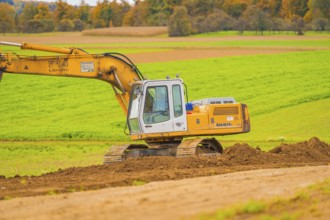 Large yellow excavator operating on an open, green area, energy revolution, construction of PV open