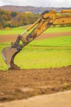 Close-up of an excavator bucket moving earth surrounded by green fields, energy transition,