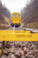 A yellow vehicle travels on rails with a Gedo CE device in the foreground, tamping machine on