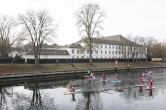 Water sports enthusiasts dressed up as Santa Claus ride SUPs on the Spree in front of Bellevue