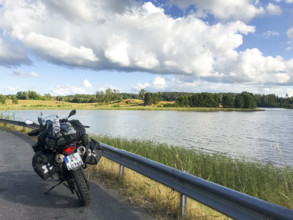 A BMW Sertao Enduro G650GS motorcycle stands on a road next to a lake under a cloudy sky surrounded